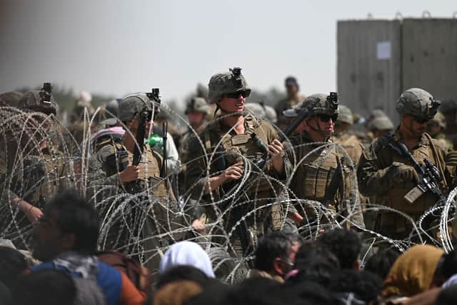 US soldiers stand guard behind barbed wire as Afghans sit on a roadside near the military part of the airport in Kabul Photo by WAKIL KOHSAR/AFP via Getty Images)