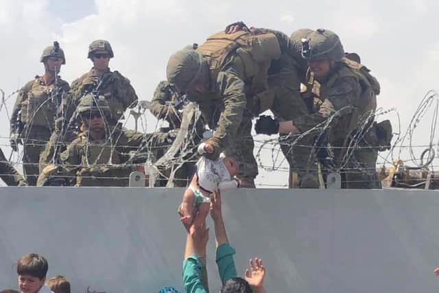 Image by Omar Haidiri shows a US Marine grabbing an infant over a fence of barbed wire during an evacuation at Hamid Karzai International Airport in Kabul Photo by OMAR HAIDIRI/Courtesy of Omar Haidiri/AFP via Getty Images)
