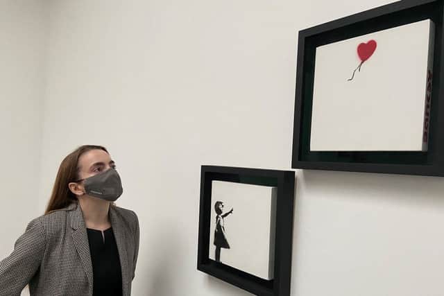 A gallery employee poses with an artwork entitled ‘Girl and Balloon’ (Diptych) by Banksy (Photo: LINDA ABI ASSI/AFP via Getty Images)