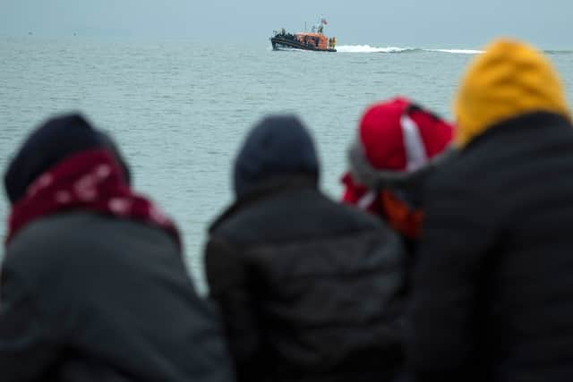 Migrants sitting on the beach look on as an RNLI (Royal National Lifeboat Institution) lifeboat carrying migrants approaches a beach in Dungeness(Photo by BEN STANSALL/AFP via Getty Images)
