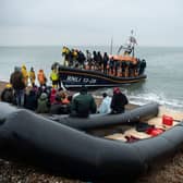 Migrants sit beside a boat used to cross the English Channel as more migrants are helped ashore from a RNLI (Royal National Lifeboat Institution) lifeboat at a beach in Dungeness, on the south-east coast of England, on November 24, 2021 (Photo: Getty)