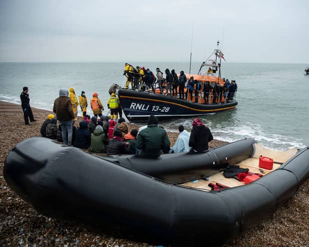 Migrants sit beside a boat used to cross the English Channel as more migrants are helped ashore from a RNLI (Royal National Lifeboat Institution) lifeboat at a beach in Dungeness, on the south-east coast of England, on November 24, 2021 (Photo: Getty)