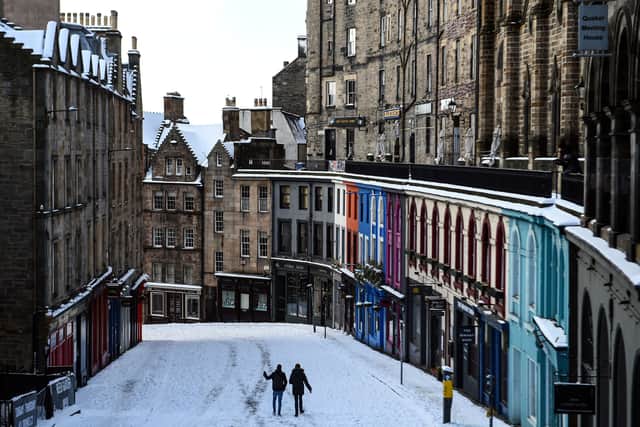 People walk in the snow on the deserted Victoria Street in Edinburgh in February this year. (Photo by ANDY BUCHANAN/AFP via Getty Images)