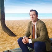 DI Neville Parker (Ralf Little) sat on a log on a beach (Credit: BBC / Red Planet / Amelia Troubridge)