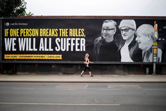 A woman walks past a billboard featuring Michael Gove, Dominic Cummings and Boris Johnson, posted by political campaign group Led By Donkeys (Photo: TOLGA AKMEN/AFP via Getty Images)