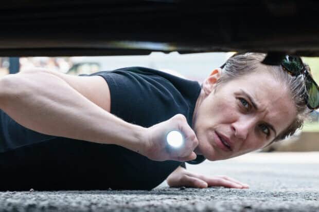 Vicky McClure lies flat on the ground, shining a torch to look under a car (Credit: Ross Ferguson/ITV)