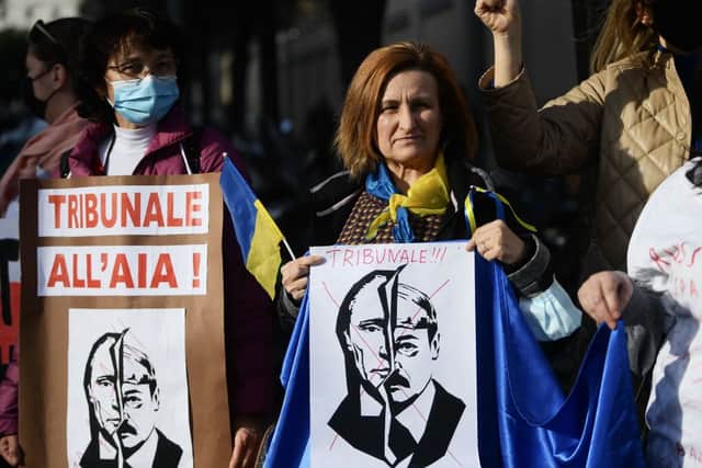 A woman holds a placard reading ‘International Criminal Court in The Hague’ above portraits of Vladimir Putin and Belarus President Alexander Lukashenko (Photo: FILIPPO MONTEFORTE/AFP via Getty Images)