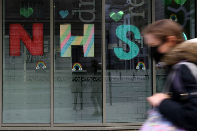 A woman wearing a protective face mask walks past messages of support for the NHS (National Health Service) in the windows of a hotel near St Thomas’ hospital in London (Photo by ISABEL INFANTES/AFP via Getty Images)