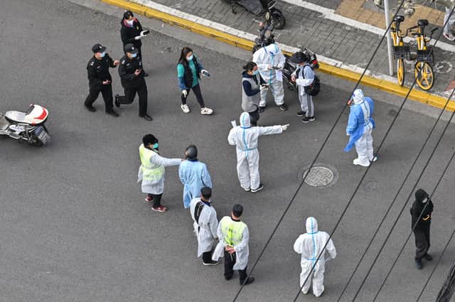 A health worker (C) wearing personal protective gear gestures to residents on a street during the second stage of a Covid-19 lockdown in Jing'an district in Shanghai on April 1, 2022.