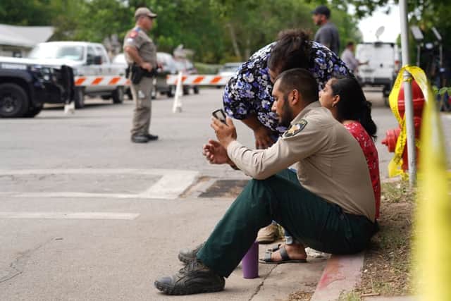 A sheriff checks his phone as he sits on the sidewalk with two women outside Robb Elementary School as state troopers monitor the area  (Photo by ALLISON DINNER/AFP via Getty Images)