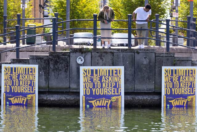 Passersby spot deliberately inconspicuous billboards positioned in the Royal Victoria Dock, Greenwich to mark the launch of the limited-edition Cadbury Twirl Caramel bar.