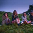 Marli Siu as Nell, Emma Appleton as Maggie, Bel Powley as Birdy, and Aliyah Odoffin as Amara, sat on the grass in the early hours of the morning (Credit: Matthew Squire/BBC/Universal International Studios)