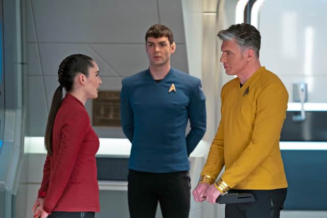 Chrissy Chong as La’an Noonien-Singh, wearing security red, Ethan Peck as Mr Spock, wearing science blue, and Anson Mount as Captain Pike, wearing command gold. They’re in deep conversation. (Credit: Marni Grossman/Paramount+)