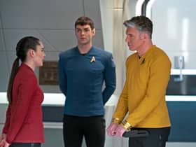 Chrissy Chong as La’an Noonien-Singh, wearing security red, Ethan Peck as Mr Spock, wearing science blue, and Anson Mount as Captain Pike, wearing command gold. They’re in deep conversation. (Credit: Marni Grossman/Paramount+)