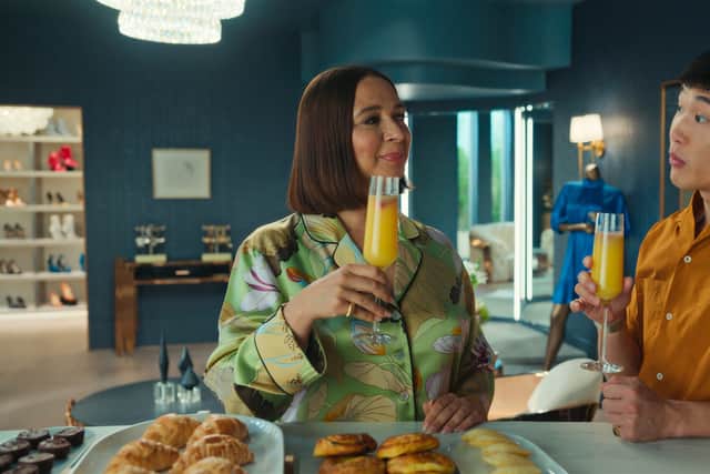 Maya Rudolph and Joel Kim Booster in Loot, holding up glasses of orange juice in front of a breakfast display (Credit: Apple TV+)