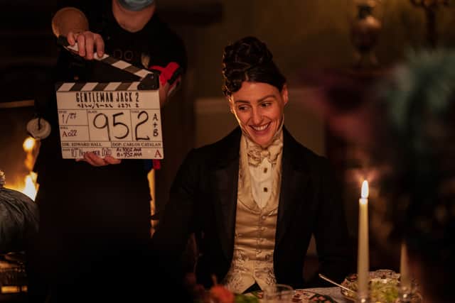 A behind the scenes image of Suranne Jones on the Gentleman Jack set, in costume smiling next to a clapperboard (Credit: BBC/Lookout Point/HBO/Aimee Spinks)