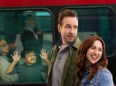 Rafe Spall as Jason and Esther Smith as Nikki, walking hand in hand past a red London bus. A child has his face pressed up against the window. (Credit: Apple TV+)