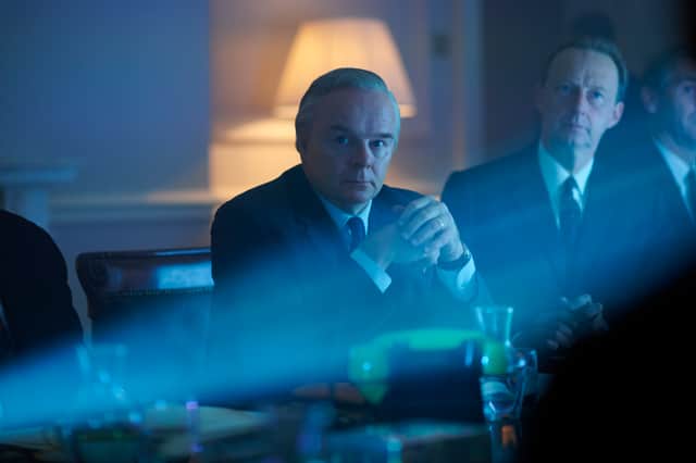 Jason Watkins as Harold Wilson in The Crown, sat at the cabinet table and illuminated by a projector (Credit: Des Willie/Netflix)
