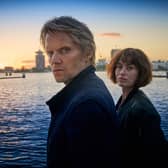 Marc Warren as Van Der Valk and Maimie McCoy as Lucienne Hassell, overlooking a canal, the sun setting behind them (Credit: ITV)