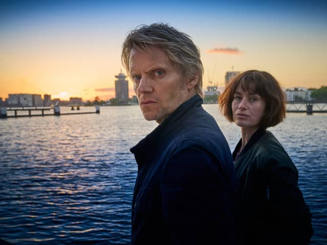 Marc Warren as Van Der Valk and Maimie McCoy as Lucienne Hassell, overlooking a canal, the sun setting behind them (Credit: ITV)