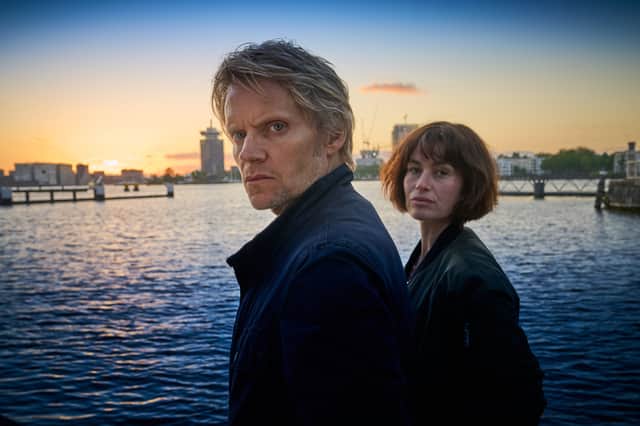 <p>Marc Warren as Van Der Valk and Maimie McCoy as Lucienne Hassell, overlooking a canal, the sun setting behind them (Credit: ITV)</p>