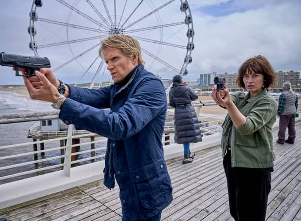 <p>Marc Warren as Van der Valk as Maimie McCoy as Lucienne, holding their guns straight ahead. They’re on a pier, with a ferris wheel behind them. (Credit: ITV)</p>