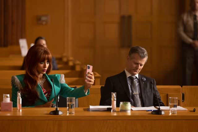 Jameela Jamil as Titania in She-Hulk: Attorney at Law. She’s wearing a turquoise blazer, taking a selfie in a courtroom, her lawyer looking frustrated beside her (Credit: Chuck Zlotnick)