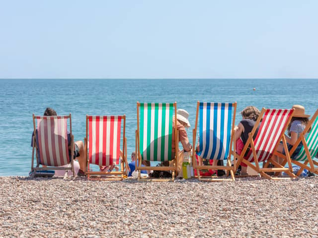 Rear View of Group of People Seated in Six Striped Deckchairs at the Seaside on a Bright Sunny Summer Day (Ian - stock.adobe.com)