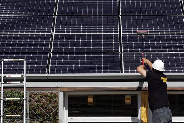 A person cleans dust off of solar panels on the roof of a home (Photo by SAUL LOEB/AFP via Getty Images)