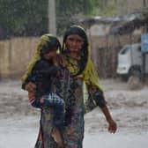 A woman carrying a child walks along a street during a heavy rainfall in the flood hit Dera Allah Yar town in Jaffarabad district, Balochistan province, on August 30, 2022. - Aid efforts ramped up across flooded Pakistan on August 30 to help tens of millions of people affected by relentless monsoon rains that have submerged a third of the country and claimed more than 1,100 lives. (Photo by Fida HUSSAIN / AFP) (Photo by FIDA HUSSAIN/AFP via Getty Images)