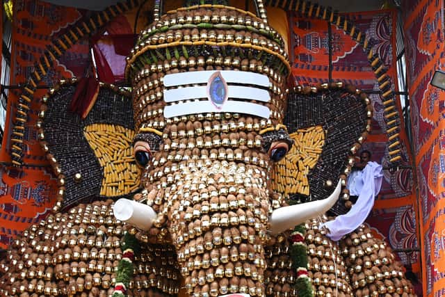 A man (R) removes a cloth to unveil a 30-feet statue of Elephant headed hindu god Ganesha made Metal pots, coconut ,corn and sugarcane at a place worship on Ganesh Chaturthi festival in Chennai on August 31, 2022.