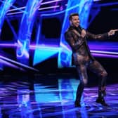 Joel Dommett gesturing wildly while hosting The Masked Dancer. He’s wearing a suit with a starfield pattern on it (Credit: ITV)