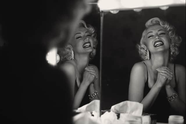 A black and white image of Ana de Armas as Marilyn Monroe, laughing in front of a three panel make-up mirror (Credit: Netflix)