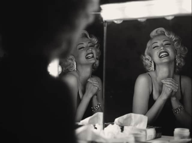 A black and white image of Ana de Armas as Marilyn Monroe, laughing in front of a three panel make-up mirror (Credit: Netflix)