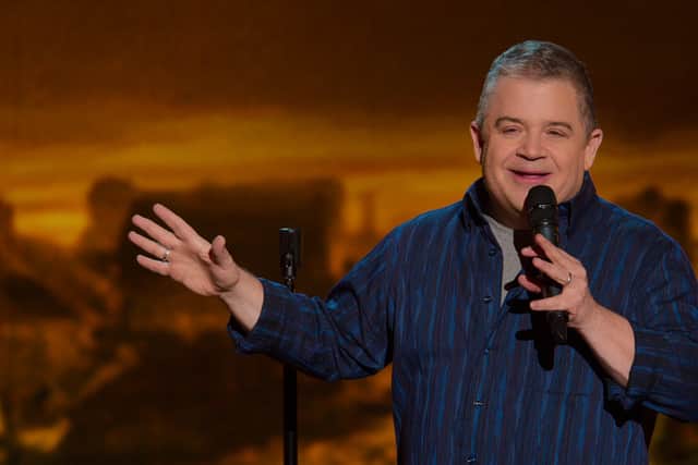 Patton Oswalt performing standup, wearing a blue button up shirt, mic in left hand and gesturing with the right (Credit: Netflix)
