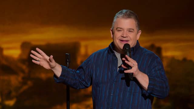 Patton Oswalt performing standup, wearing a blue button up shirt, mic in left hand and gesturing with the right (Credit: Netflix)
