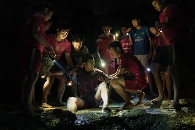 The teenagers of the Thai fotball team, trapped in a dark, damp cave. They’re gathered around one of their teammates, helping him up, illuminated by torchlight  (Credit: Sasidis Sasisakulporn)