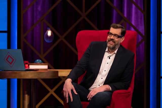 Richard Osman, sat in a big red armchair with a blue laptop computer to his left, hosting Richard Osman’s House of Games Night (Credit: BBC/Remarkable TV/Graeme Hunter)