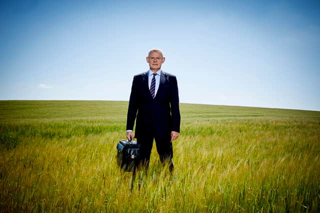 Martin Clunes as Doc Martin Ellingham, stood holding a briefcase in a field of long grass (Credit: ITV)