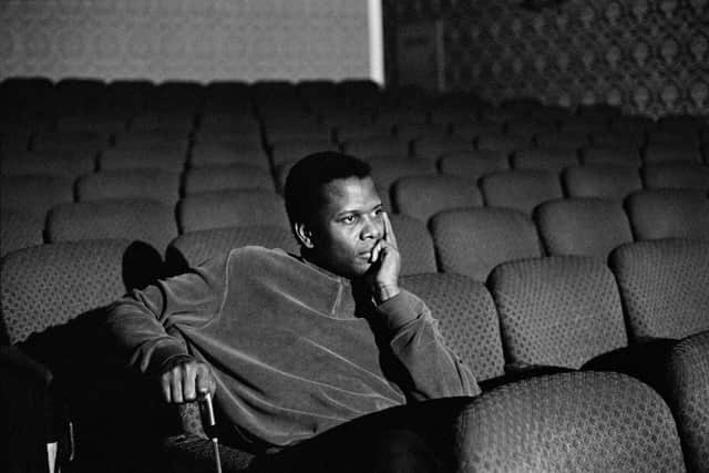 A black and white photo of a young Sidney Poitier, sitting alone in a small cinema room, looking thoughtful (Credit: Apple TV+)