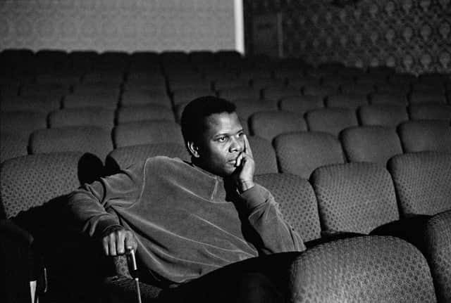 A black and white photo of a young Sidney Poitier, sitting alone in a small cinema room, looking thoughtful (Credit: Apple TV+)