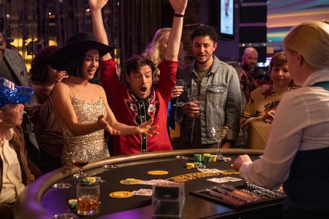 Rosa Salazar as Katie McConnell and Gavin Drea as Steffan Bridges in Wedding Season. They’re celebrating at a blackjack table, and she is wearing a cowboy hat (Credit: Greg Gayne/Disney+)