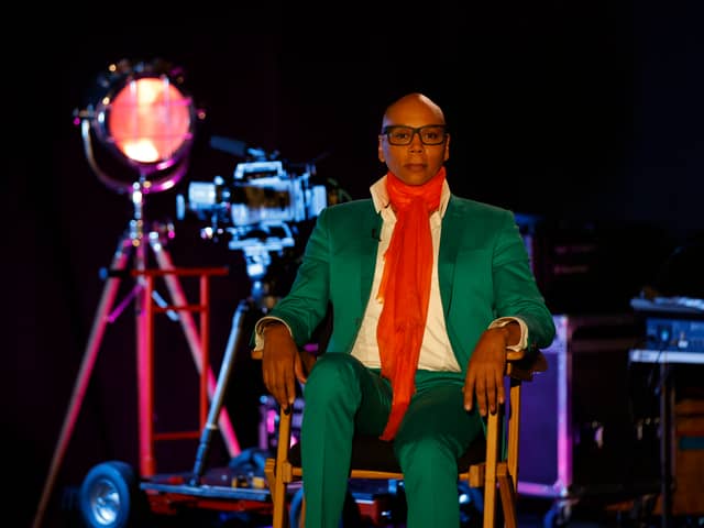 RuPaul is a drag megastar wearing a green suit and orange scarf with a large lamp in the background