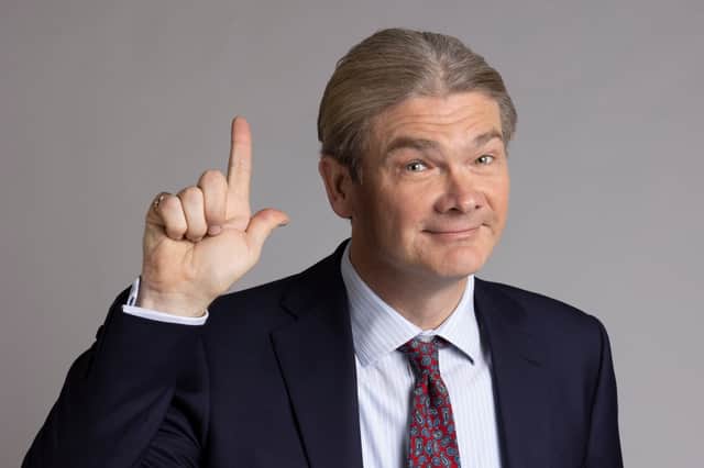 Simon Farnaby as Julian Fawcett MP in Ghosts, wearing a suit and holding his left hand up in an L shape (Credit: BBC/Monumental/Guido Mandozzi)