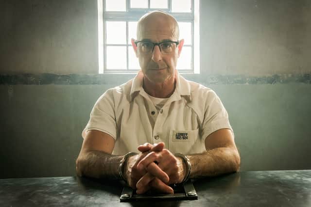 Stanley Tucci as Jefferson Grieff in Inside Man, wearing a white prison jumpsuit and handcuffed to a table (Credit: BBC/Hartswood/Kevin Baker)