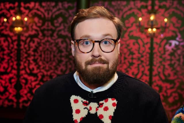 John Kearns on Taskmaster, wearing glasses and a black knit jumper with a red and white bowtie design (Credit: Rob Parfitt / Channel 4)
