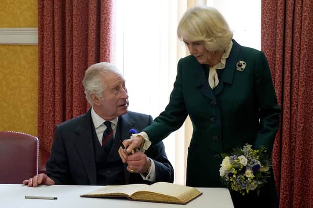 Britain's King Charles III (L) and Britain's Camilla, Queen Consort hold a pen as they sign a visitors' bok after attending an official council meeting at the City Chambers in Dunfermline
