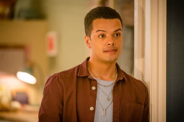 Dylan Brady as Danny in Ralph & Katie, stood in a doorway. He’s wearing a brown shirt over a grey t shirt, with some silver chain jewellery (Credit: BBC/ITV Studios)