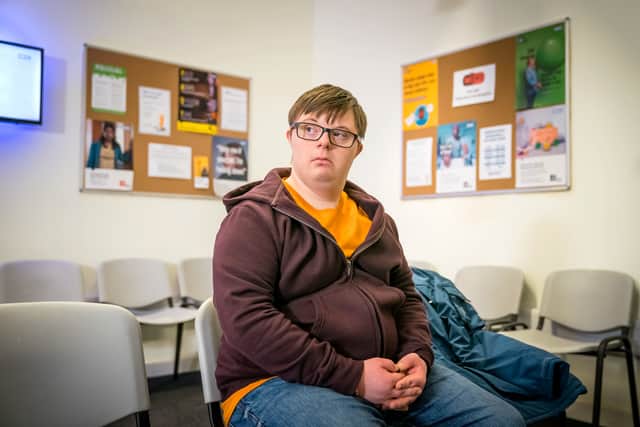 Leon Harrop as Ralph in Ralph & Katie, sat alone in a doctor’s waiting room. He’s wearing a brown zip jumper over an orange t-shirt, and looks concerned (Credit: BBC/ITV Studios)