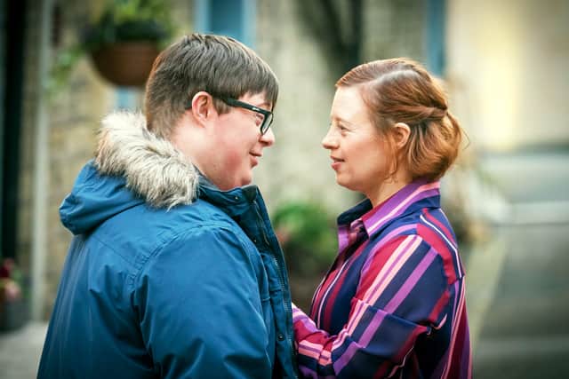 Leon Harrop as Ralph and Sarah Gordy as Katie in Ralph & Katie, stood outside the bakery looking into each other’s eyes. He’s wearing a thick blue coat and she is wearing a red and purple striped shirt (Credit: BBC/ITV Studios/Ben Blackall)